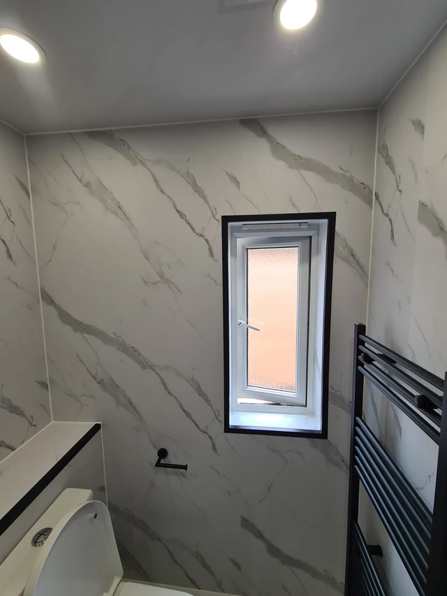 Marble-effect panelled wall with a small black-framed window, a black towel radiator and spotlights in the ceiling