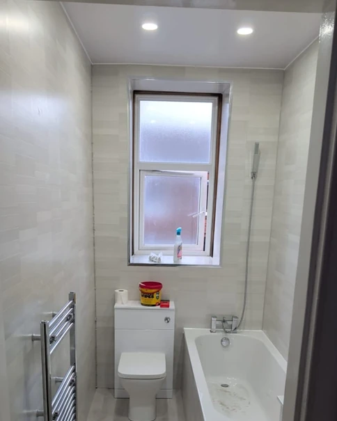 Bathroom after the refit: new wall panels, a WC with a unit, a heated towel rail and a window