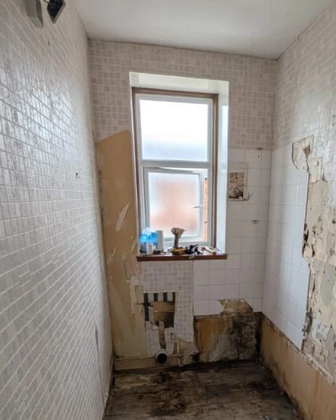 Bathroom before the refit: old tiled walls and peeling wallpaper, bare floorboards and a window